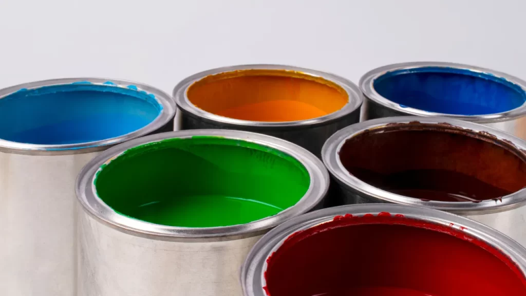 Latas de tinta metálicas abertas, contendo diferentes cores vibrantes — azul claro, laranja, azul escuro, verde, marrom e vermelho.